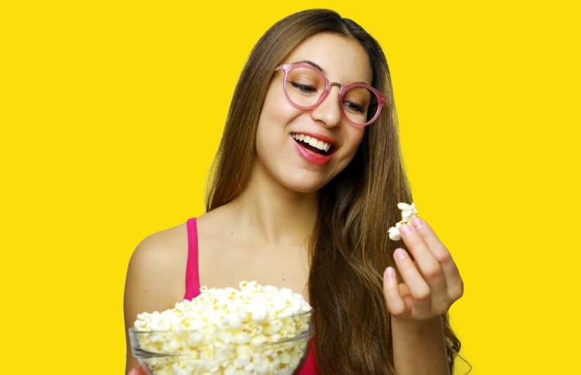 Young Woman Eating Popcorn Against Yellow Background